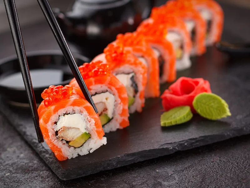 Salmon sushi roll topped with salmon roe, picked up by black chopsticks