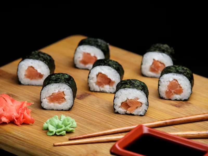 Small salmon maki rolls on bamboo board with pickled ginger and wasabi