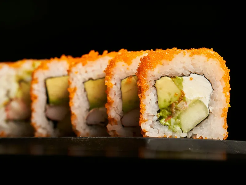 Sushi roll covered with orange tobiko, filled with avocado and crab meat