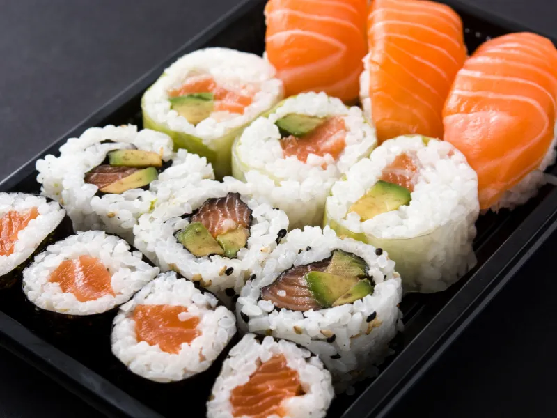 Take‑out sushi box with salmon nigiri and various avocado maki rolls